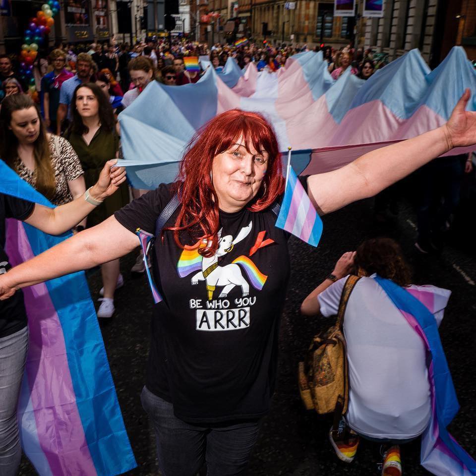 Kate posing and smiling in front of giant trans flag